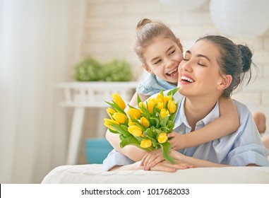 Happy mother's day! Child daughter is congratulating mom and giving her flowers tulips. Mum and girl smiling and hugging. Family holiday and togetherness. - Powered by Shutterstock