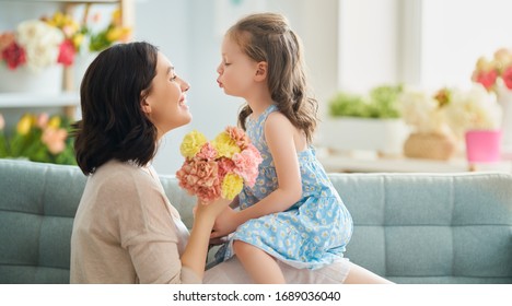 Happy mother's day! Child daughter congratulates mom and gives her flowers. Mum and girl smiling and hugging. Family holiday and togetherness.                                - Shutterstock ID 1689036040