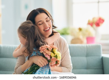 Happy mother's day! Child daughter congratulates mom and gives her flowers. Mum and girl smiling and hugging. Family holiday and togetherness. - Shutterstock ID 1689036046