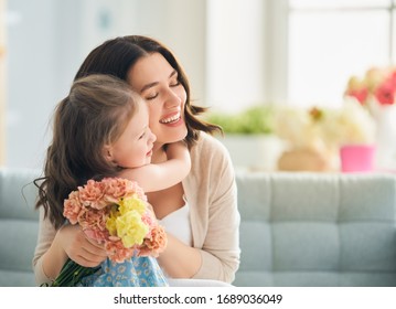 Fröhlicher Muttertag! Kindertochter gratuliert Mutter und gibt ihr Blumen. Mama und Mädchen lächeln und umarmen. Familienurlaub und Zusammensein.                               