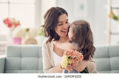 Happy mother's day! Child daughter congratulates mom and gives her flowers. Mum and girl smiling and hugging. Family holiday and togetherness.  - Shutterstock ID 1695391033