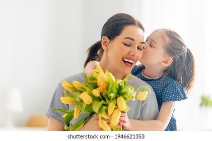 Happy mother's day. Child daughter congratulates mom and gives her flowers. Mum and girl smiling and hugging. Family holiday and togetherness. - Shutterstock ID 1946621353
