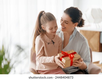 Happy mother's day. Child daughter is congratulating mom and giving her gift box. Mum and girl smiling and hugging. Family holiday and togetherness. - Powered by Shutterstock