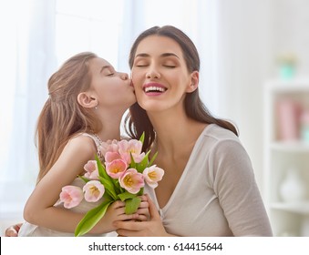 ¡Feliz día de la madre! La hija pequeña felicita a su madre y le da tulipanes de flores. Mamá y chica sonriendo y abrazándose. Vacaciones familiares y unión. Foto de stock