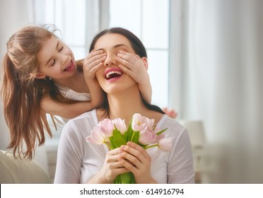 Happy mother's day! Child daughter congratulates mom and gives her flowers tulips. Mum and girl smiling and hugging. Family holiday and togetherness. - Powered by Shutterstock