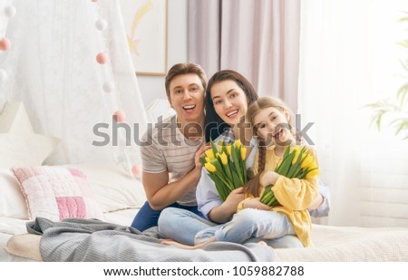 Happy mother's day! Child daughter with dad congratulating mom and give her flowers tulips. Family holiday and togetherness.
