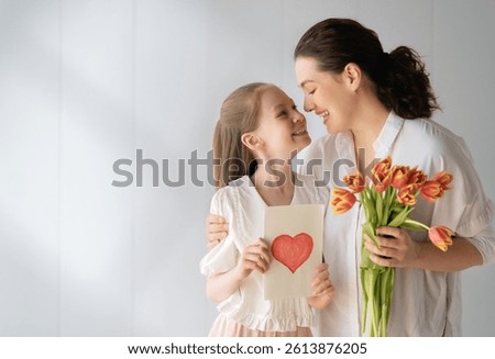 Happy mother's day! Child daughter is congratulating mom and giving her flowers tulips. Mom and girl smiling on white background. Family holiday and togethernes