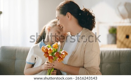 Happy mother's day. Child daughter is congratulating mom and giving her flowers. Mum and girl smiling and hugging. Family holiday and togetherness.