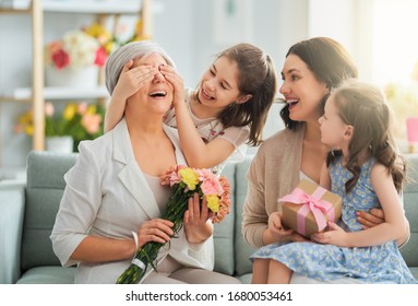 Happy Mother's Day! Children Daughters Are Congratulating Mom And Granny Giving Them Flowers And Gift. Grandma, Mum And Girls Smiling And Hugging. Family Holiday And Togetherness.       