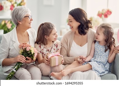 Happy Mother's Day! Children Daughters Are Congratulating Mom And Granny Giving Them Flowers And Gift. Grandma, Mum And Girls Smiling And Hugging. Family Holiday And Togetherness. 