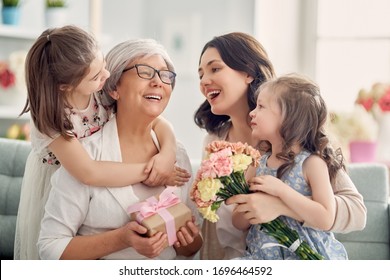 Happy Mother's Day! Children Daughters Are Congratulating Mom And Granny Giving Them Flowers And Gift. Grandma, Mum And Girls Smiling And Hugging. Family Holiday And Togetherness. 