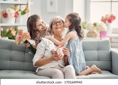 Happy mother's day! Children daughters are congratulating granny giving her flowers and gift. Grandma and girls smiling and hugging. Family holiday and togetherness.                                