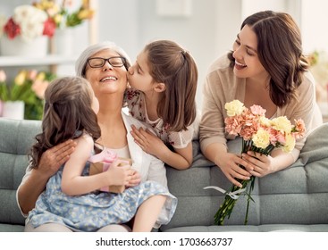 Happy Mother's Day! Children Daughters Are Congratulating Mom And Granny Giving Them Flowers And Gift. Grandma, Mum And Girls Smiling And Hugging. Family Holiday And Togetherness.