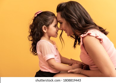 Happy Mothers Day! Close Up Portrait Of A Beautiful And Charming Mother And Daughter With Beaming Smiles On Yellow Background. Eskimo Kisses Daughter And Mother