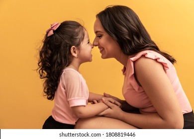 Happy Mothers Day! Close Up Portrait Of A Beautiful And Charming Mother And Daughter With Beaming Smiles On Yellow Background. Eskimo Kisses Daughter And Mother