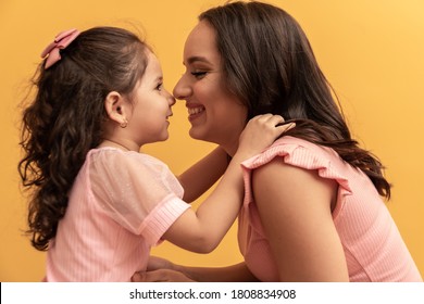 Happy Mothers Day! Close Up Portrait Of A Beautiful And Charming Mother And Daughter With Beaming Smiles On Yellow Background. Eskimo Kisses Daughter And Mother