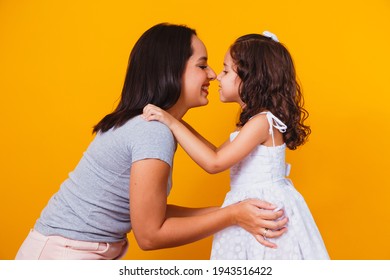 Happy Mothers Day! Close Up Portrait Of A Beautiful And Charming Mother And Daughter With Beaming Smiles On Yellow Background. Eskimo Kisses Daughter And Mother