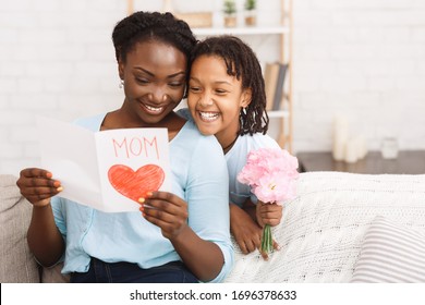 Happy Mother's Day Concept. Black child greeting her mom with flowers and card, copyspace