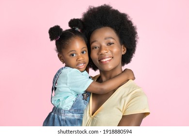 Feliz día de la madre, familia, concepto de maternidad. Fotografía de estudio de cerca de la feliz y bella joven madre africana, sosteniendo a su linda hija, posando ante la cámara con fondo rosado Foto de stock