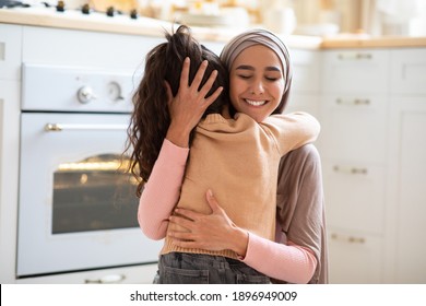 Happy Mother's Day. Little Girl Cuddling Tight Her Muslim Mom In Kitchen At Home, Expressing Love And Affection. Positive Islamic Woman In Hijab Hugging Her Child And Smiling, Closeup With Copy Space