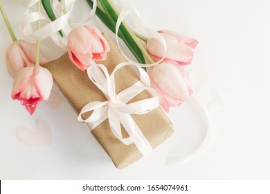 Happy Mothers Day. Pink Tulips Flat Lay With Ribbon And Gift Box On White Background. Stylish Soft Image Of Spring Flowers. Happy Womens Day. Greeting Card Mockup.  Hello Spring