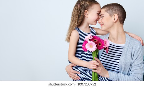 Happy Mother's Day, Women's day or Birthday background. Cute little girl giving mom bouquet of pink gerbera daisies. Loving mother and daughter smiling and hugging. 