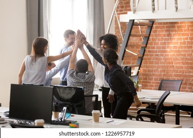 Happy motivated diverse office team giving high five together, excited multi-ethnic employees group celebrating reward, startup success, good teamwork result, engaging in teambuilding concept