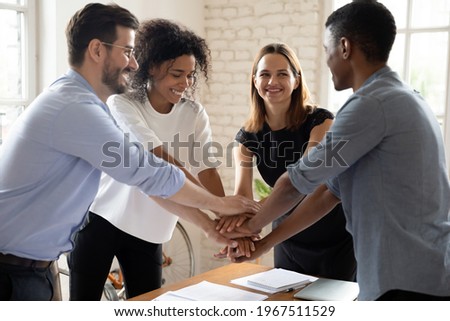 Happy motivated young mixed race diverse colleagues employees joining hands together, showing company staff unity, celebrating professional achievement or successful teamwork, cooperation concept.