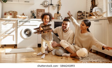 Happy Multi Ethnic Family: Little Boy Laughing And Playing With   Toy Airplane In Front Of His  His Parents In The Kitchen At Home
