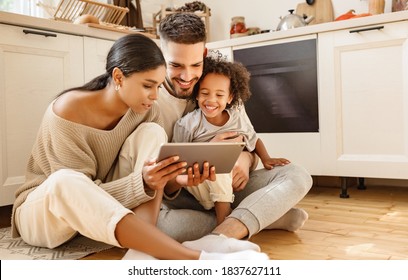 happy multi ethnic family: parents and little son watching cartoon on tablet on weekend day  while sitting on the kitchen floor at home together 
 - Powered by Shutterstock