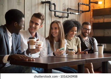 Happy Multi Ethnic Group Of Friends Talking Using Smartphones In Cafe, Diverse Young People Laughing Having Fun At Coffee Break In Coffeehouse, Cheerful Millennials Enjoying Meeting In Coffeeshop