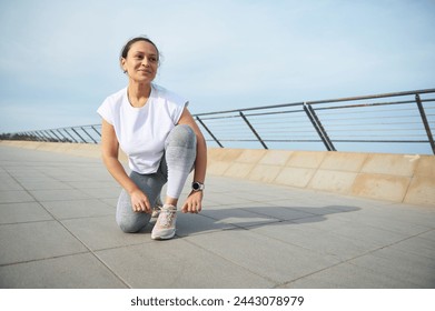 Happy multi ethnic woman runner tying laces on sports shoes, smiling looking away, getting ready for morning run on the promenade. Running nd jogging concept. People. Active healthy lifestyle. Sport - Powered by Shutterstock