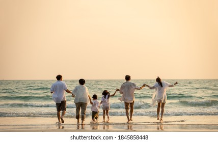 Happy multi generation Asian family holding hands and walking on the beach together at summer sunset. Smiling big family parents with child boy and girl enjoy in outdoors lifestyle travel vacation