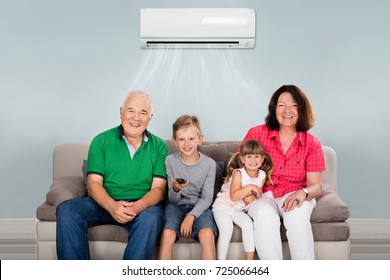 Happy Multi Generation Family With Two Kids Watching Television Under Air Conditioning At Home