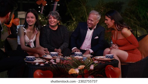 Happy multi generation Indian family sitting chair around dining table enjoy night dinner spending time together. Group diverse people having fun communicating each other eating meal outside home  - Powered by Shutterstock