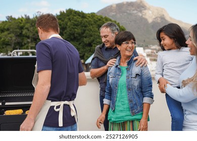 Happy multi generational family having fun doing barbecue lunch at house rooftop - Grandparents, parents and child - Focus on senior woman face - Powered by Shutterstock