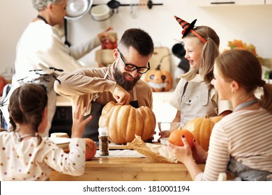 Happy Multi Generational Family Smiling And Carving Jack O Lantern From Pumpkin While Gathering Around Table During Halloween Celebration
