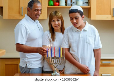 Happy multi racial jewish family lighting candles celebrating Jewish holiday Hanukkah. Jewish Dad, Mom and teenager son or grandparents with grandson lighting Chanukkah Candles in menorah for holidays