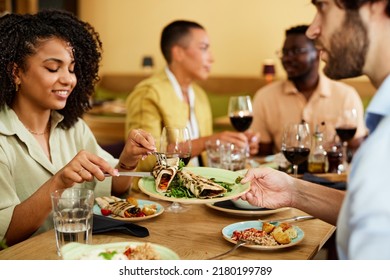 A Happy Multicultural Couple Sits In A Restaurant With Their Friends And Eats Dinner.