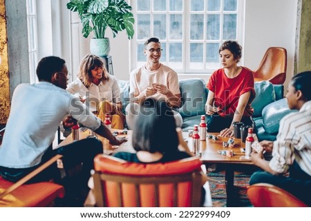 Happy multicultural hipster guys playing in gambling sitting at table with poker chips and cards, smiling diverse friends 20s spending time for together entertainment practice blackjack gaming