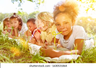 Happy Multicultural Kids Drink Water With Straw In Summer On A Meadow