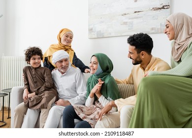 happy multicultural muslim family looking at smiling girl while sitting on couch at home