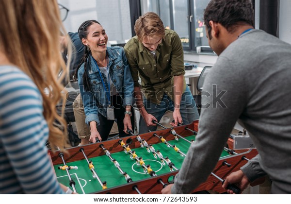 happy multicultural people playing in table soccer\
at modern office