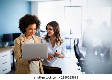 Happy multiethnic business women working together online on a laptop in corporate office.