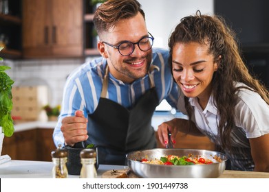 Happy Multiethnic Couple Cooking Homemade Tomato And Basil Pasta. Cooking At Home