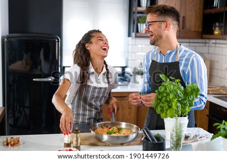 Happy multiethnic couple cooking homemade tomato and basil pasta. Cooking at home