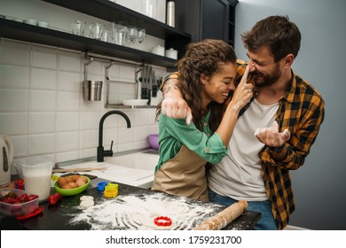 Happy multiethnic couple cooking in their kitchen. They are making cookies. - Powered by Shutterstock