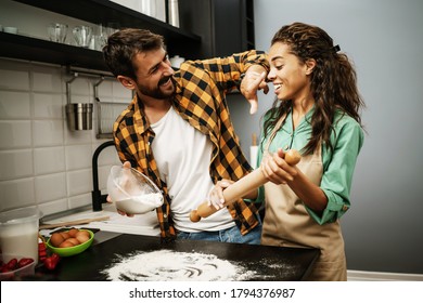 Happy multiethnic couple cooking in their kitchen. They are making cookies. - Powered by Shutterstock