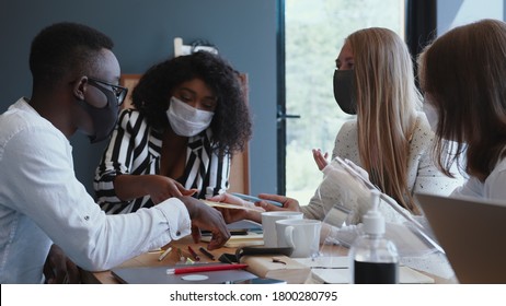 Happy multiethnic development company business people consulting customers at light office table wearing face masks.
