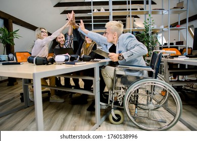 Happy multiethnic diverse young people sitting in office and giving high five each other after great collaboration, discussing strategies. Disabled male manager sitting with his colleagues at office - Powered by Shutterstock